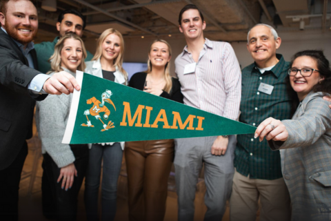 Group of University of Miami alumni holding Miami pennant flag